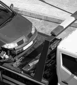 Une photo en noir et blanc d'une voiture épave en cours de remorquage sur le dos d'un camion porte voiture.